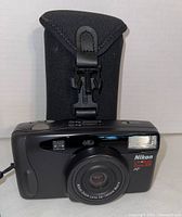 Front view of Nikon Light Zoom 105 camera with lens extended and carrying case behind.