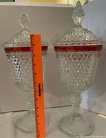 Photo of two clear pressed glass candy jars with diamond pattern, fitted lids, pedestal bases, and a measuring ruler showing height approximately 12 inches.