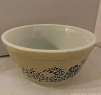 Photo of a small vintage Pyrex bowl with tan exterior and blue floral pattern