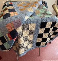 Patchwork quilt featuring various traditional quilt blocks and multiple colors draped over a surface, showing textile texture and stitching detail.