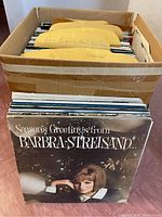 Top-down view of a cardboard box filled with vinyl records, with visible paper dividers separating sections, and the front album is 'Season’s Greetings from Barbra Streisand.'