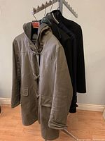 Four jackets hanging on a clothing rack, front jacket is gray with toggles and hood