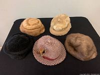 Photo of five vintage ladies hats arranged on black background, showing variety of fur and wool materials, and decorative elements