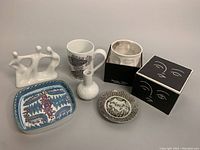 Complete lot showing all 6 items on a gray surface: white porcelain sculpture, decorated mugs, small vase, box with face illustration, small plates.