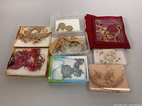 Photo showing multiple jewelry sets in boxes and storage bags, including gold-toned, silver-toned, pink/red stone sets.