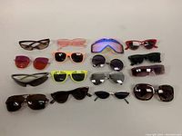 Top-down view of 15 assorted sunglasses arranged on a beige surface, showing diverse styles and colors.