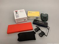 Various tools and devices including boxed Datacolor ColorReader, boxed BOSS SD-1 pedal, Silstar Grapho8 case, magnifying glasses, caliper case