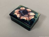 Top-side view of rectangular ceramic box with domed lid featuring raised flower design in greens, pinks, and purples.