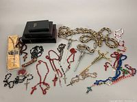 Photo showing collection of rosary beads in various colors and styles, several crucifixes, and a small booklet.