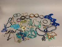 Group shot showing all jewelry items including necklaces, bangles, and bracelets in various colors and materials spread out on white background.