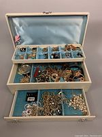 Full view of vintage jewelry box with open top lid and two drawers pulled out showing assorted jewelry inside compartments and drawers.