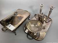 Overview of multiple silver plated pieces including rectangular serving dish with lid, baking dish insert, candleholders, coffee pot, handled tray, and footed bowl with grid insert