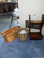 Two woven baskets and wooden wall shelf placed on carpeted floor in front of a white wall.