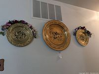 Three brass colonial wall plates mounted on the wall each with floral accents