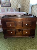 Front view of a dark wood chest with four faux drawers and white knobs, placed in a bedroom next to a bed with floral bedding.