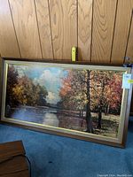 Framed vintage landscape print featuring a river and autumn-colored trees, showcasing overall condition and frame details.