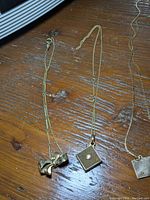 Three chain jewelry items on wooden surface: bow pin, 14K pendant with pearl, plain square pin