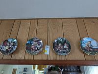 Wide shot of all four vintage Hummel plates hung on a wooden wall, showing artwork and size.