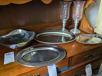 Wide view of the lot showing 4 metal trays and 2 pewter candlesticks with hurricane globes on wooden dresser.