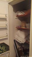 Closet with folded white linens on wooden shelves and storage containers