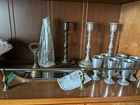 Photo of metal candlestick holders, pewter goblets, pewter serving tray, and two metal bells including one bottle opener bell.