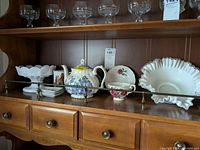 Wide view of shelf displaying milk glass bowls, porcelain teapot, Royal Staffordshire tea cup and saucer, and dipping trays.