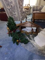 Photo showing the nativity manger with figurines wrapped in white cloth and straw inside, along with a small artificial Christmas tree decorated with pine cones and a red star on top placed next to the manger.
