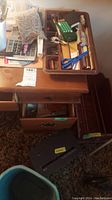 Wide view of the wooden desk with the wooden tray holding assorted office supplies and the black shredder on the floor beside the desk.