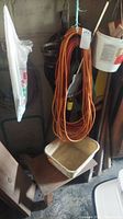 Photo of long orange extension cord hanging on a wall, with a white bucket and wood blocks below.