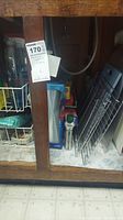 Under cabinet photo showing metal wire racks, cleaning bottle, and boxed items within the cabinet space.