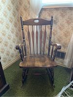 Front view of the wooden rocking chair showing spindle back, armrests, and curved rockers.