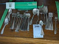 Photo showing a collection of silver plated appetizer forks, demitasse spoons and a box of International Stainless spoons on a wooden surface