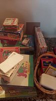 Photo showing stacked boxes containing card games, puzzles, a wooden block set, and a model car kit. A basket with smaller items is also visible.