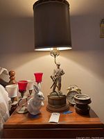 Full view of the lamp with Civil War soldier figure, the rabbit figurine, red and white votive candle holders, gold alarm clock and brown ceramic piece on wooden surface.