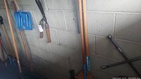 Wide view of various yard tools including shovels and snow shovel hanging against a cinder block wall.