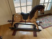 Side view showing the full carved wooden rocking horse on a wooden rocker base, highlighting the horsehair tail, painted hooves, and saddle.