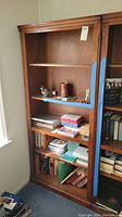 Full view of wooden bookcase with some items on shelves and blue painter's tape on one shelf.