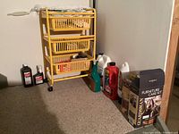 Yellow plastic rolling utility cart with four drawered baskets, various bottles of cleaning and medical supplies to the right on floor.