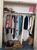 Closet with assorted women's jackets and pants hung on hangers, some in garment bags with shoes below