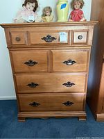 Front view of the wood dresser showing four drawers and decorative metal pulls. Dolls and a vase are on top but not included in the lot.