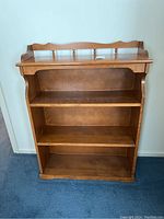 Front view of wood hutch top bookshelf with three shelves and decorative top rail with spindles.