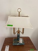 Front view of the lamp showing the green stone base, brass metal accents, and white rectangular cloth shade with torn interior.