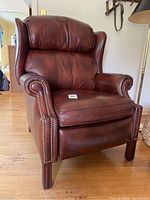 Front view of leather wingback recliner showing rolled arms, nailhead trim, wood legs