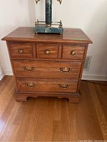 Front view of wooden end table with three drawers and brass handles, surface showing scratches.