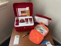 Photo of the red Clarins Super Restorative skincare case containing a serum bottle, cream jar, two small tubes, a bottle of toning lotion, along with an orange travel organizer with skincare sachets, a white and red Clinique pouch, and two small cosmetic brushes on a wooden table.