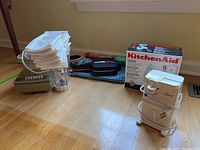 Overview image showing the grouped kitchen appliances and napkins together on floor, including the blender, can opener, napkins, a pan, and boxed KitchenAid mixer.