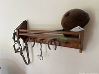 Oak wall shelf with mounted horse bridle, horseshoes, riding crop, and riding helmet.
