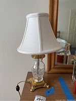 Full view of Waterford crystal table lamp with white shade on wooden surface in front of mirror.