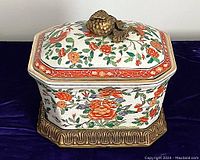 Three-piece lidded porcelain coffer with brass stand, decorated with colorful hand-painted flowers and birds, topped with gilt knob.