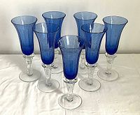Seven blue hand-blown glass flutes arranged in a group on a white surface, showing overall look and quantity.